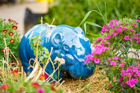 A blue ceramic hippo surrounded by a variety of flowers.