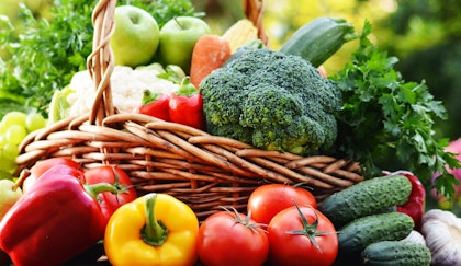 An assortment of fresh vegetables in and around wicker basket and sitting in a sunny outdoor setting
