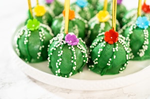 A dish of colorful, cactus-shaped cake pops with colorful flowers on them.