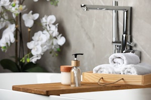 A closeup of a free-stanind tub with a wooden tray, towels and spa accessories, and a large white orchid in the background.