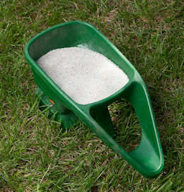 A close up of a container used to hand fertilize a lawn laying on top of a lawn.