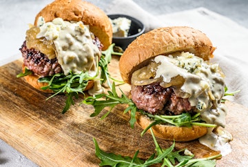 Two blue cheese burgers on a cutting board.