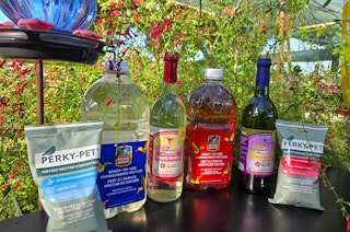 Six different hummingbird nectar varieities, with a hummingbird feeder and plants in the background.