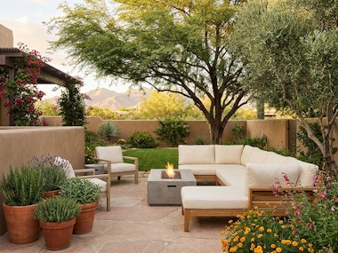 A modern backyard in the southwest with comfortable seating, a fire pit, potted herbs, colorful flowers, native trees and a small lawn.