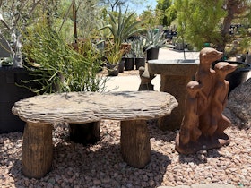 A stone bench, next to a stone birdbath, and a statue of three animals standing together.