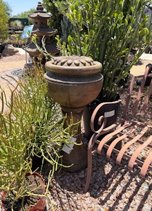 Bubbler Fountain surrounded by plants, near a metal fountain, and with a Pagoda in the background.