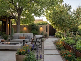 A shaded Southwest patio with a seating area, potted flowers, raised garden bed, apple tree and accent lighting.