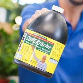 A SummerWinds staff member holding a large bottle of SUPERthrive vitamin solution for plants.