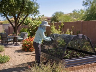 A woman adding shade cloth to her raised garden bed in her Southwest backyard.