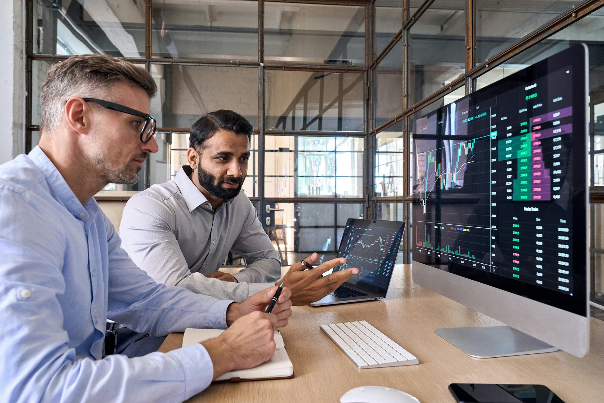 Two businessmen looking at a computer screen with buy/sell data