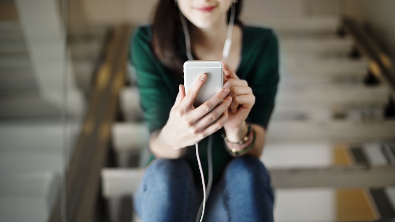 Vrouw zit op trap en luisterd naar een podcast op haar mobiel
