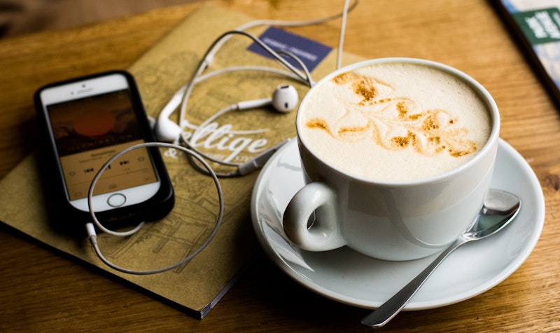 Mobiel met podcast ligt naast een kopje koffie