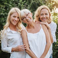 Three women smiling at the camera all wearing white blouses.