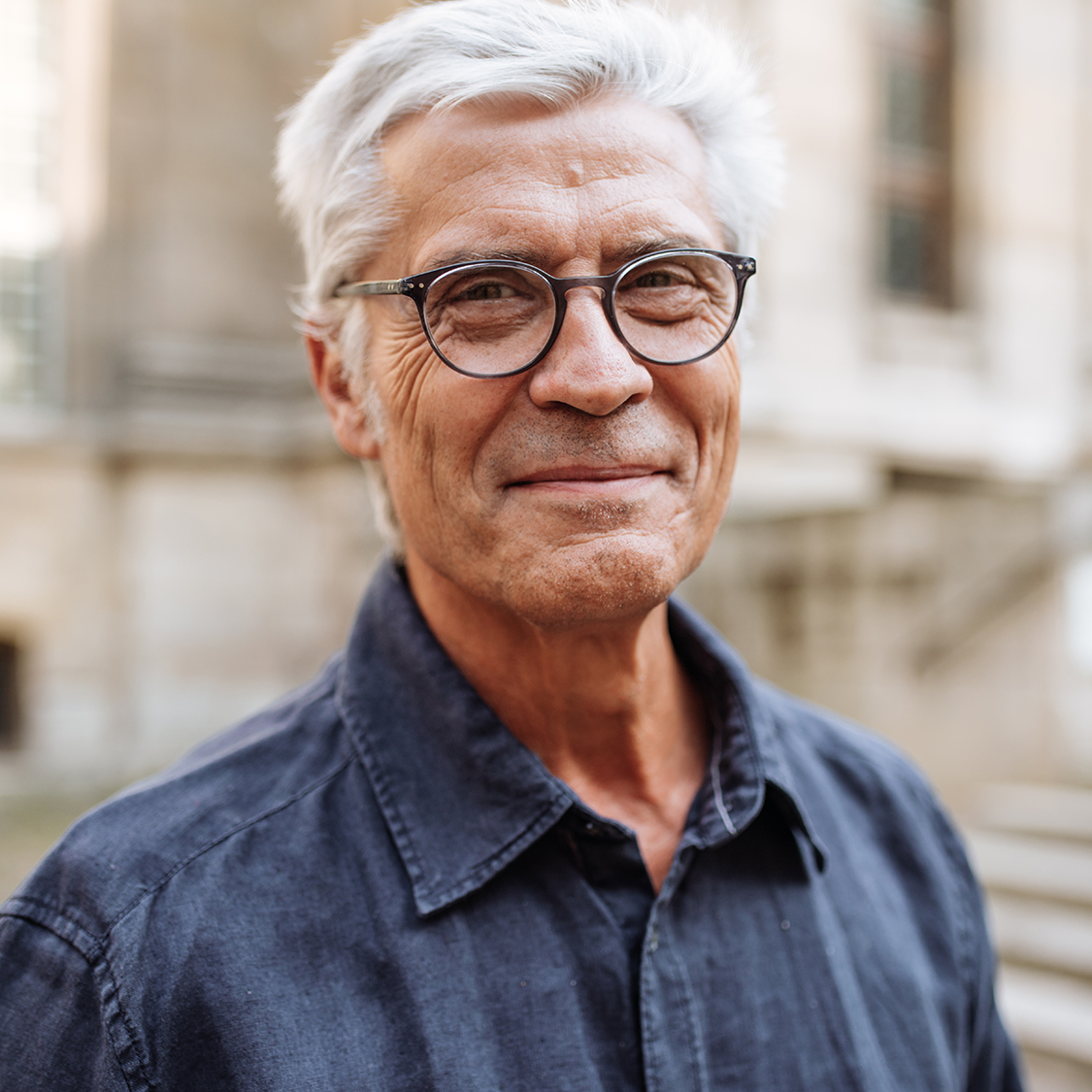 Middle aged man smiling at the camera, wearing glasses and a navy shirt. 