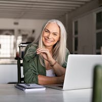 Woman smiling while working on computer, taking off her glasses.