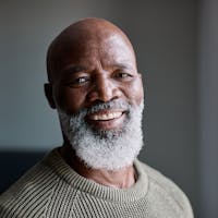 Man smiling at camera, with a grey beard and olive sweater.