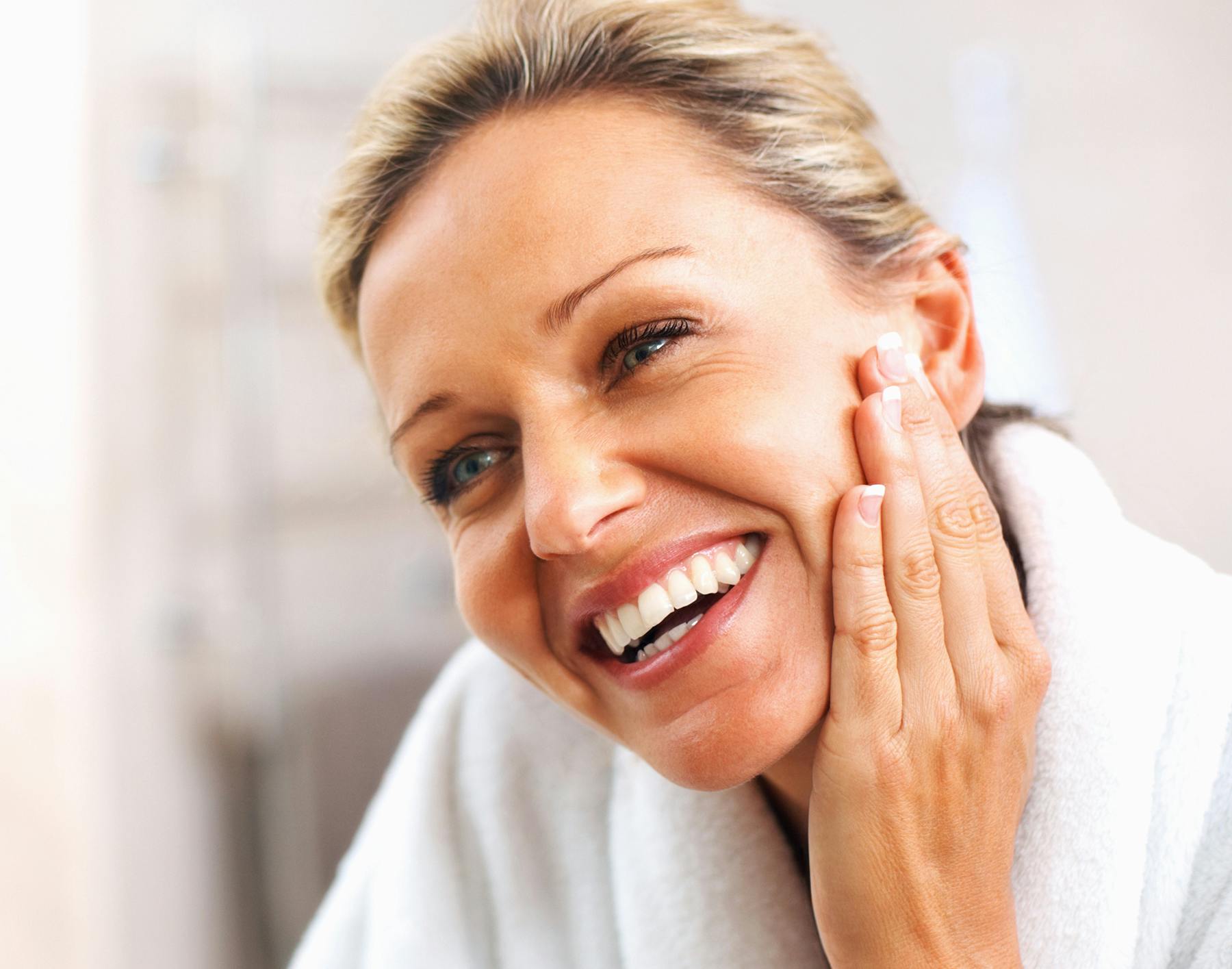 smiling woman in white robe holding her hand to her face