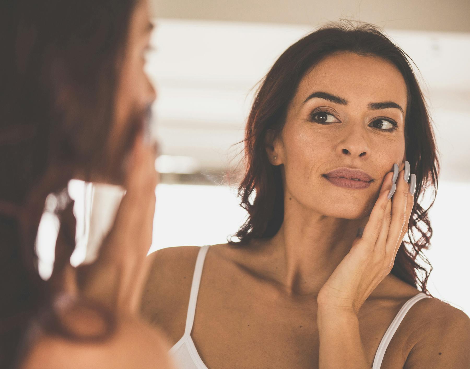 woman looking in the mirror at her face and looking at her skin