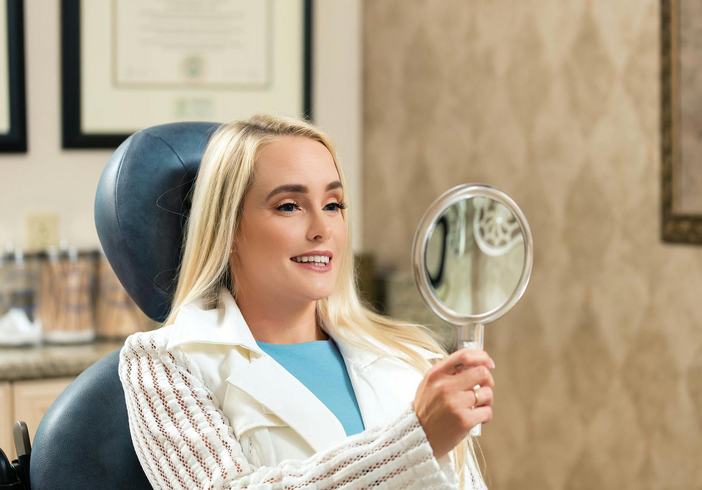 blond woman in a chair holding a mirror and smiling