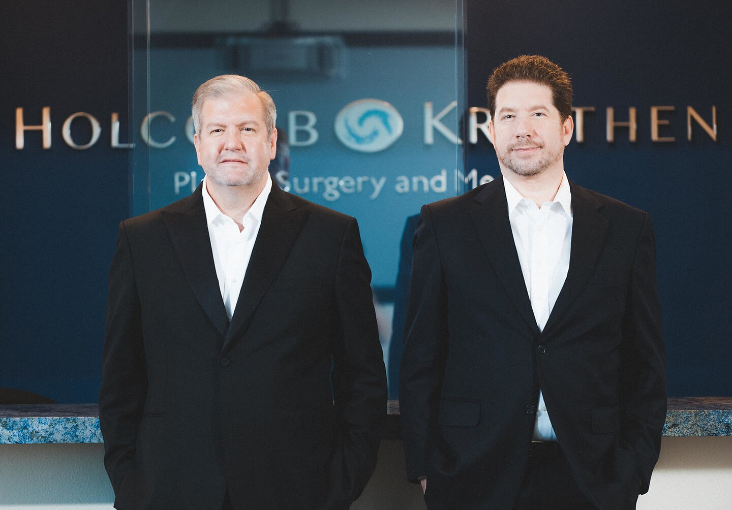 two men in suits standing in front of a blue counter