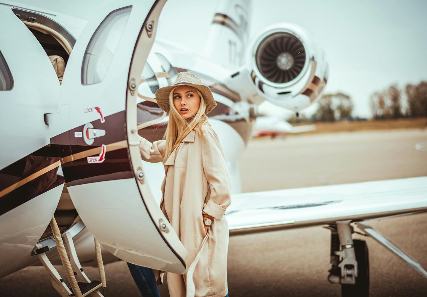 woman in a trench coat standing in front of a private jet