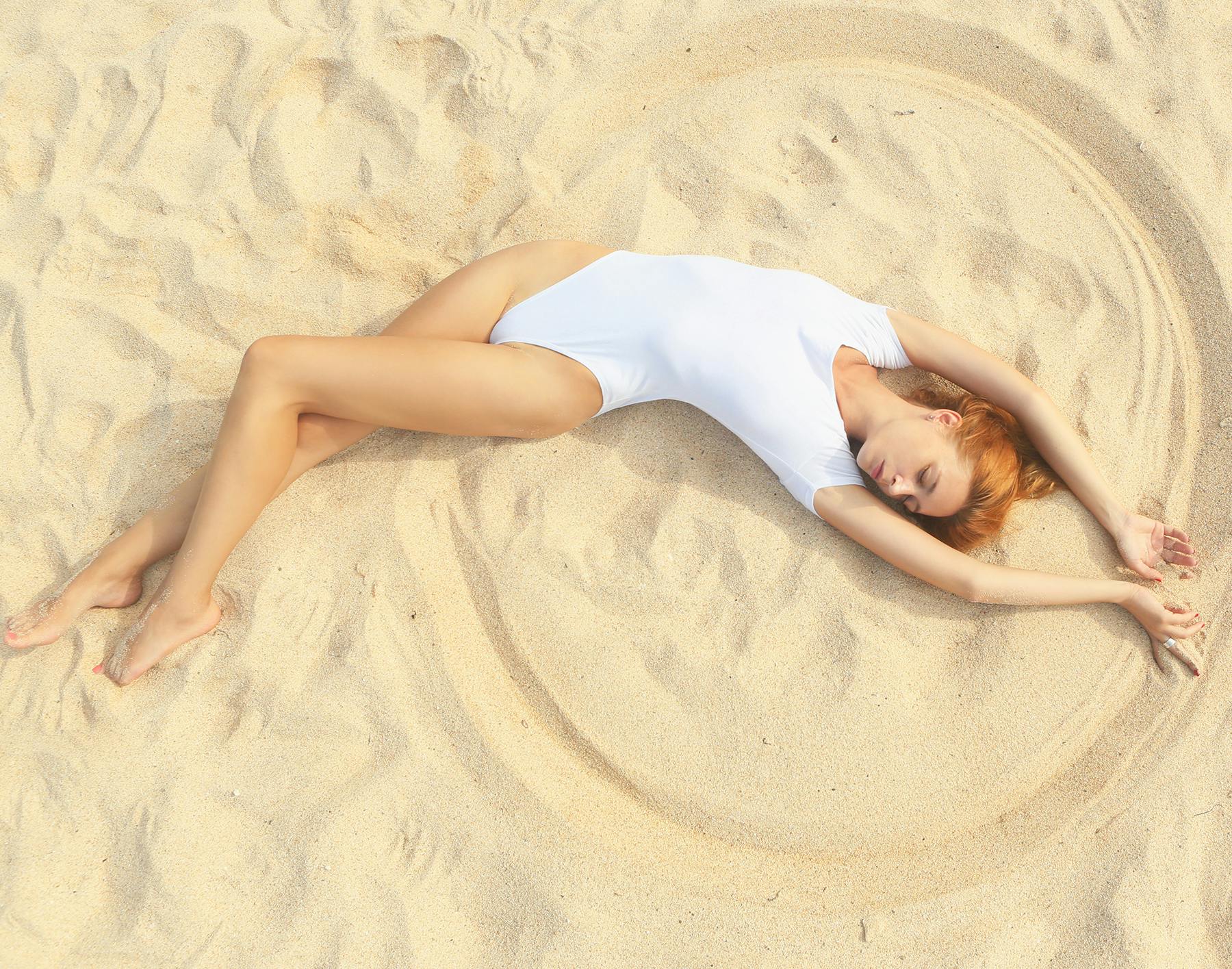 woman laying on the beach in a white bodysuit