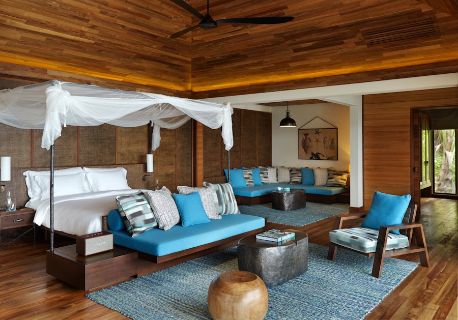 A bedroom behind floor-to-ceiling glazing, open to the ocean.