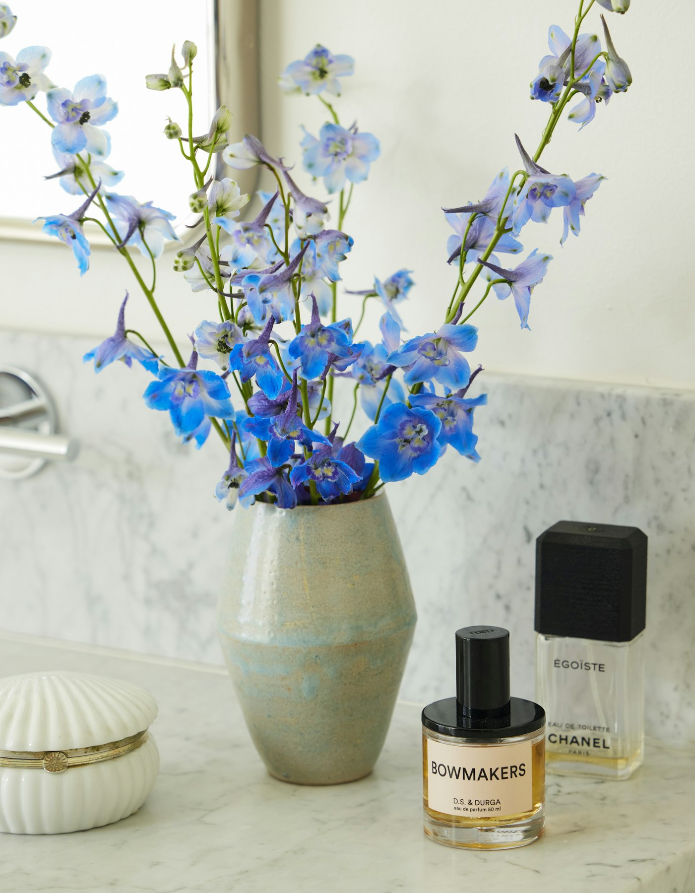 flowers in vase standing on bathroom counter with perfume bottles