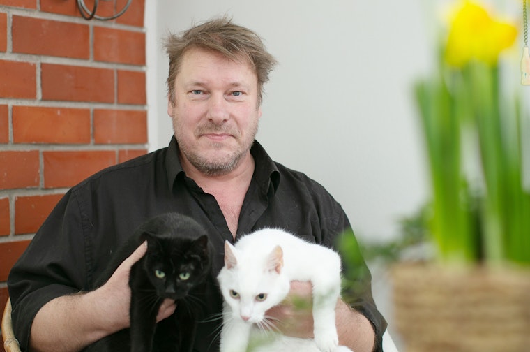 Kari Andrejeff istuu parvekkeellaan ja hänen sylissään on musta ja valkoinen kissa.  