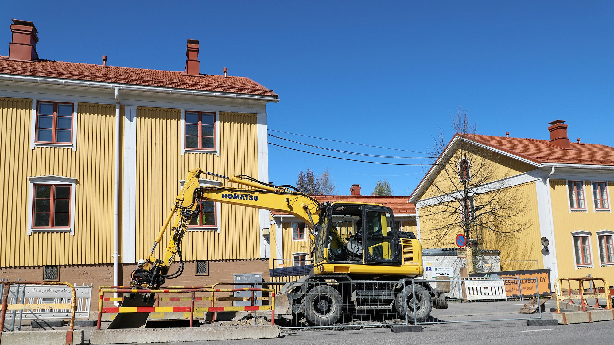 Kuvassa keltaisia puutaloja ja edessä keltainen kaivinkone. Kohteen perusparannus alkanut.