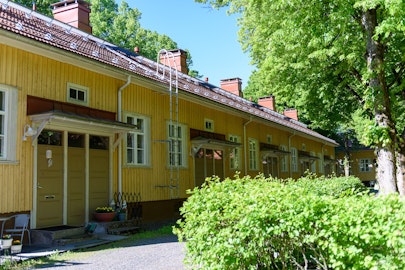 Kurjenmäenkadun keltainen talo kesällä, puut ja pensaat vihertävät.