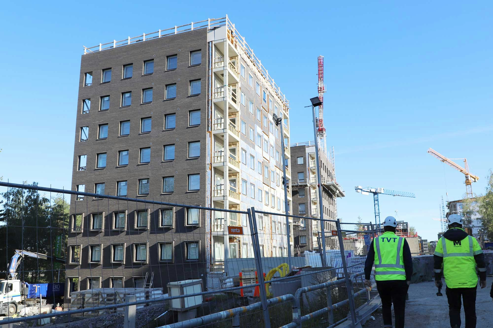 Linkkitorninkatu 7:n kaksi kerrostaloa rakentuvat Jaaninojan viereen.  Oikealla kävelee kaksi henkilöä, joilla  TVT:n ja Mangroven keltaiset turvaliivit.
