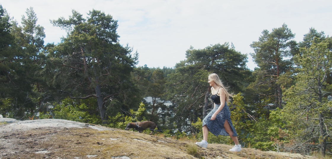Nainen kävelemässä Arolan kallioisilla metsäpoluilla, taustalla pilkottaa meri.