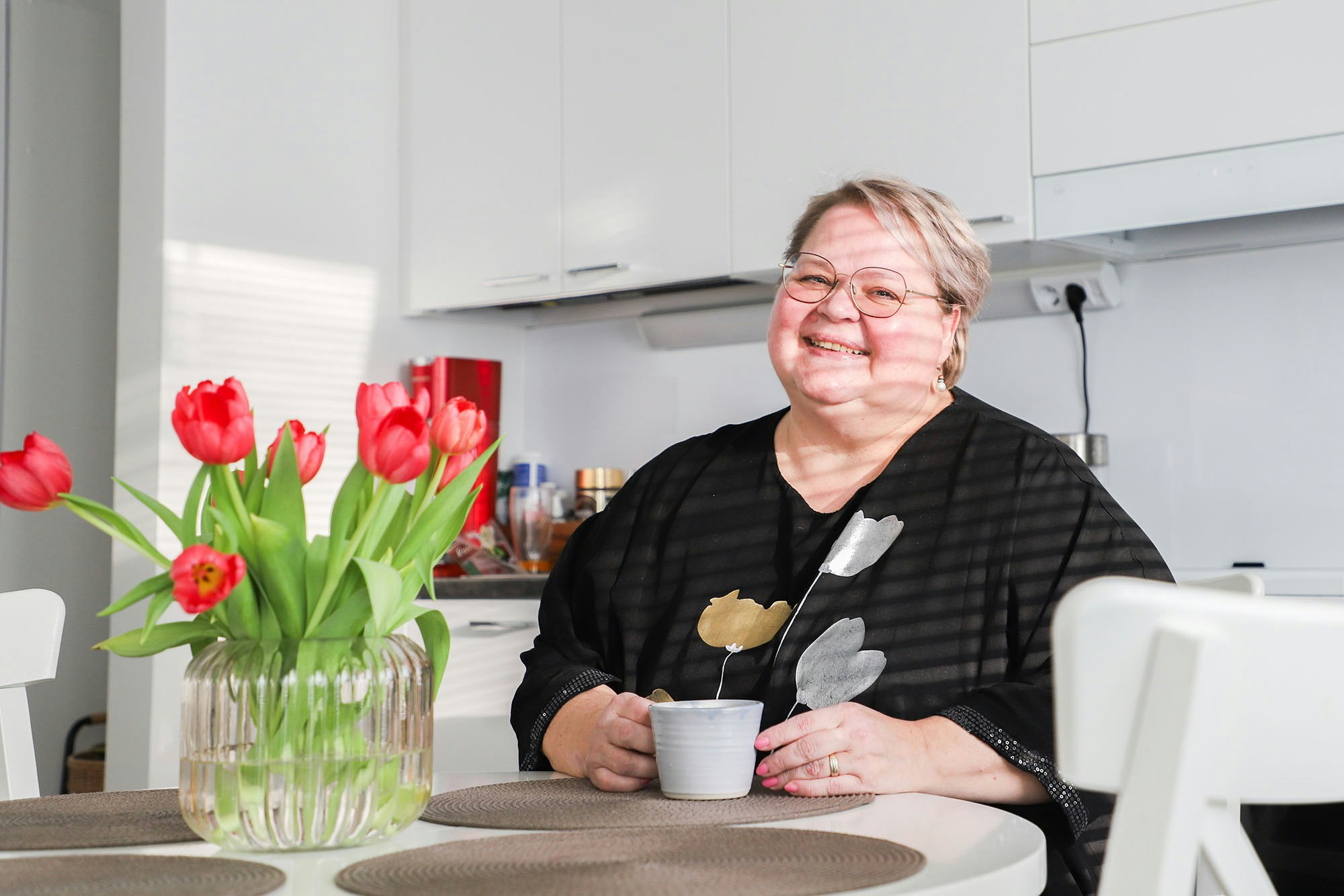 Henkilö istuu keittiön pöydän ääressä ja hymyilee.