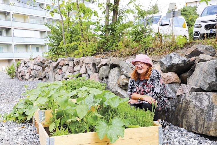 Henkilö on kyykyssä istutuslaatikoiden vieressä ja hymyilee.