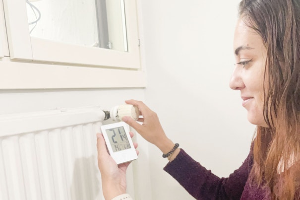 Henkilö säätää patterin termostaattia ja katsoo lämpötilamittaria.