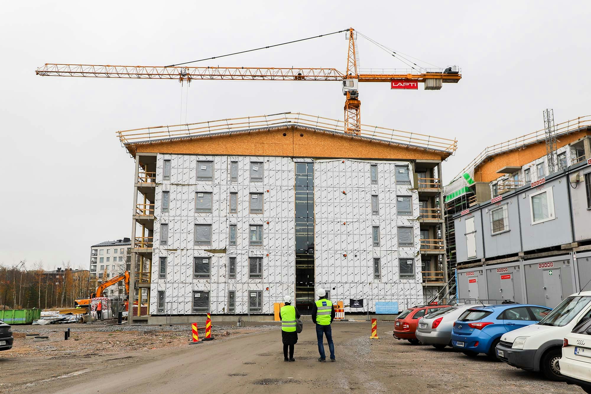 Henkilöt seisovat katsomassa rekenteilla olevaa kerrostaloa.