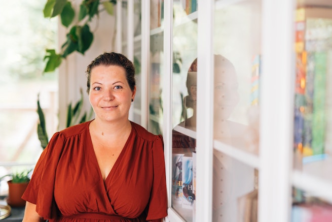 Krista Luotonen nojaa kirjahyllyyn