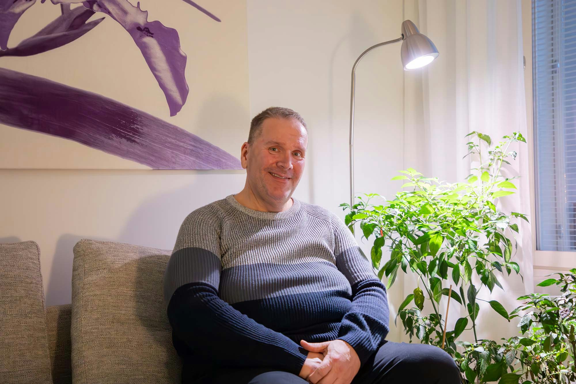 Henkilö istuu sohvalla ja hymyilee.