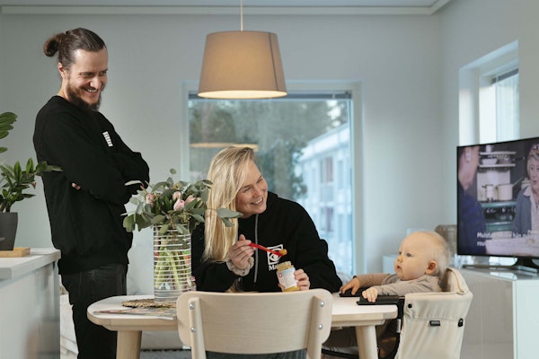 Kaksi aikuista ja vauva keittiön pöydän ääressä.