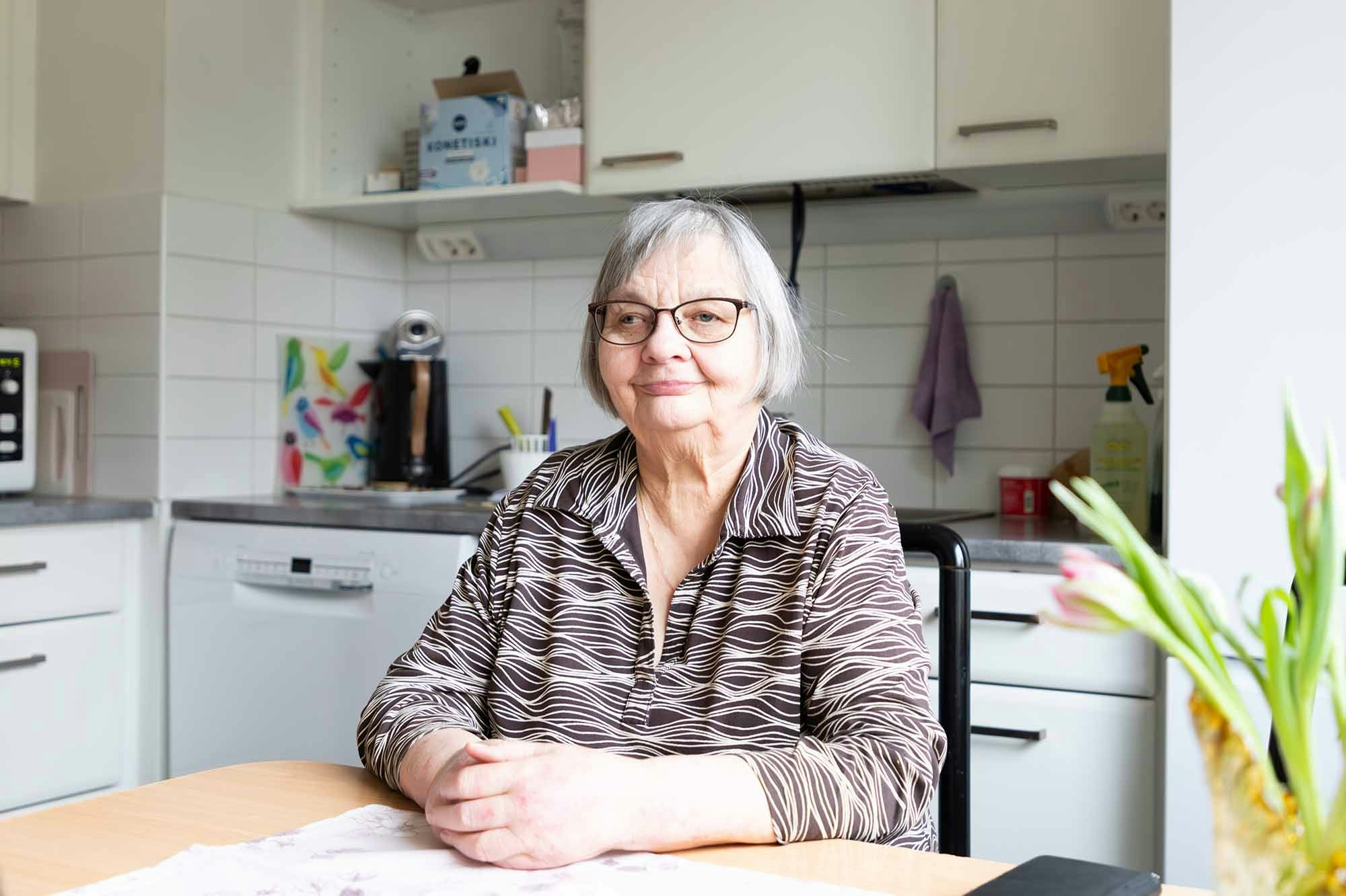 Henkilö istuu keittiön pöydän ääressä ja hymyilee.