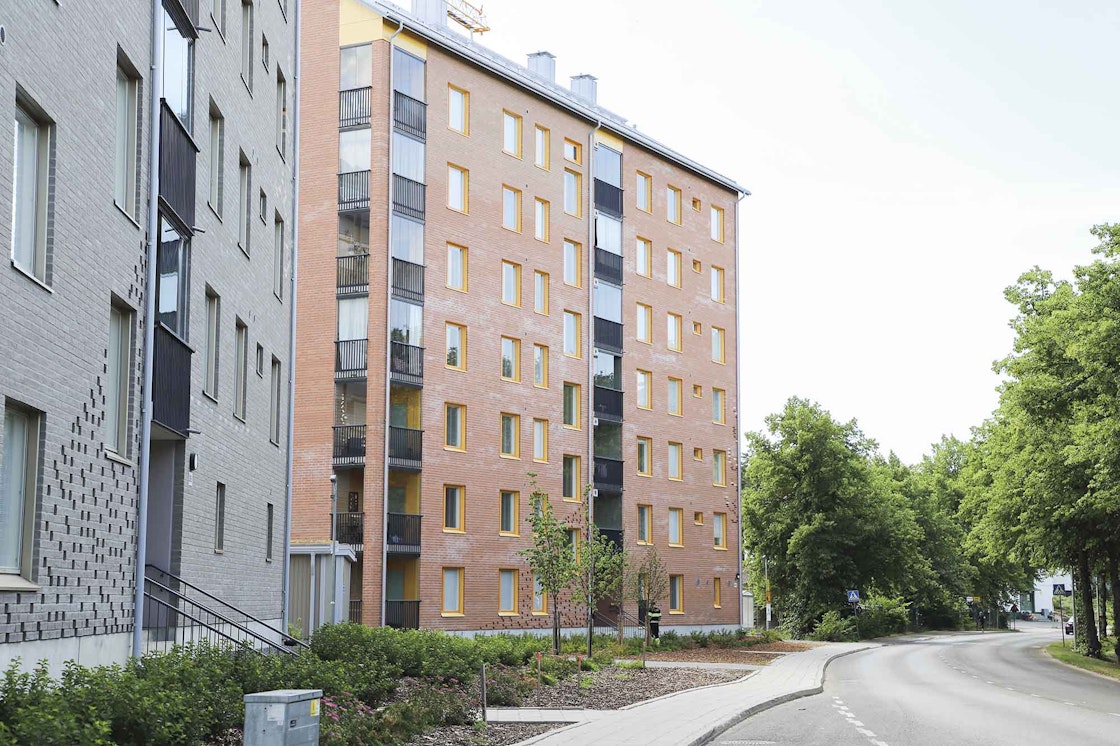 Harmaa- ja punatiiliset kerrostalot autotien vieressä.