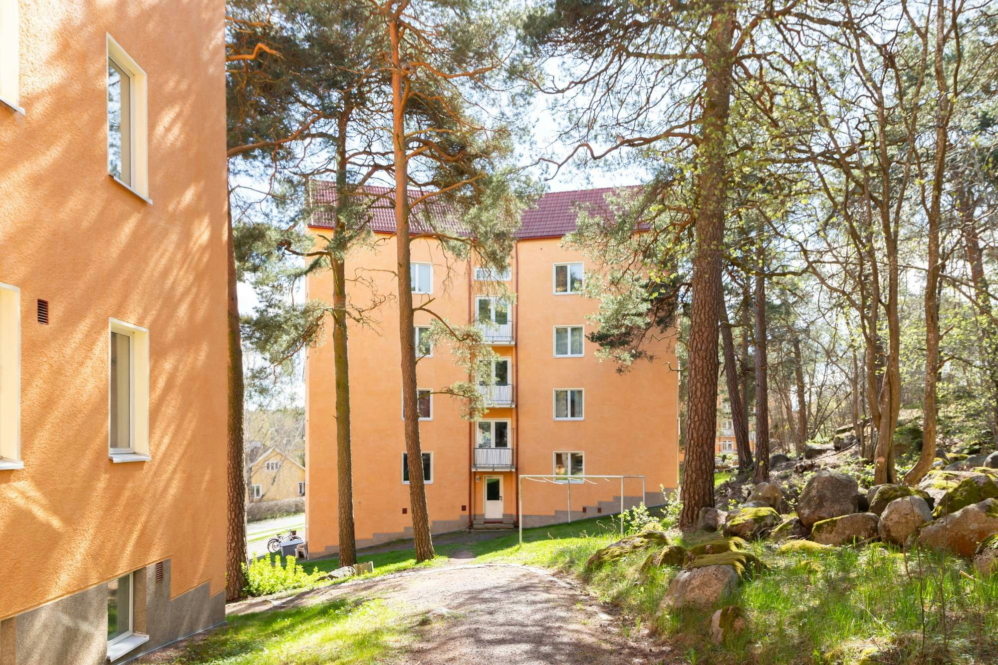 Oranssi kerrostalo punaisella tiilikatolla mäntyjen ympäröimänä.