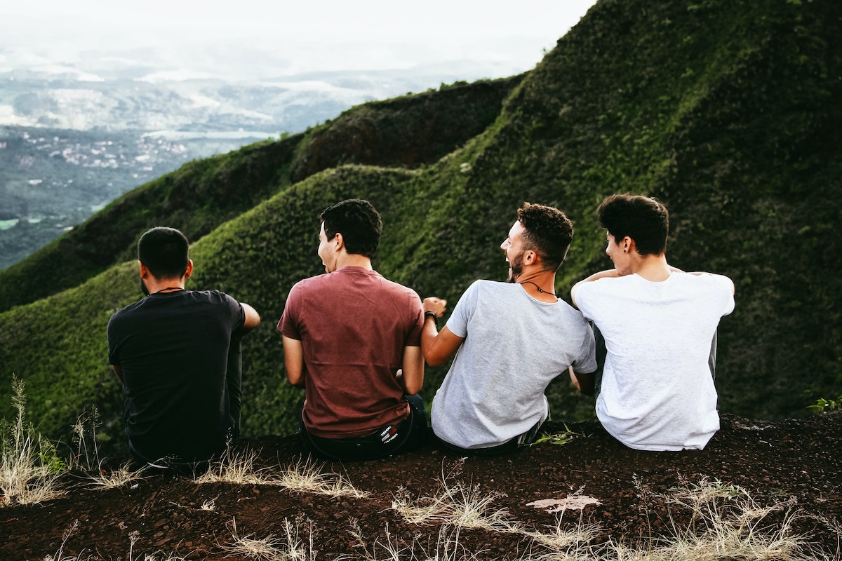 group of friends talking to each other and sitting on the ground watching a mountain in front of them.
