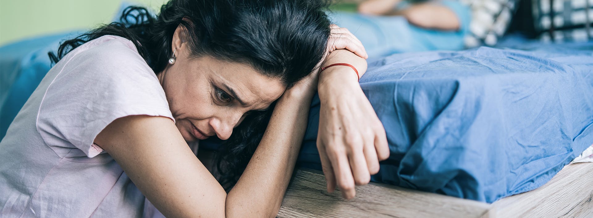 there is a woman that is sitting on a bed with her head on her hands