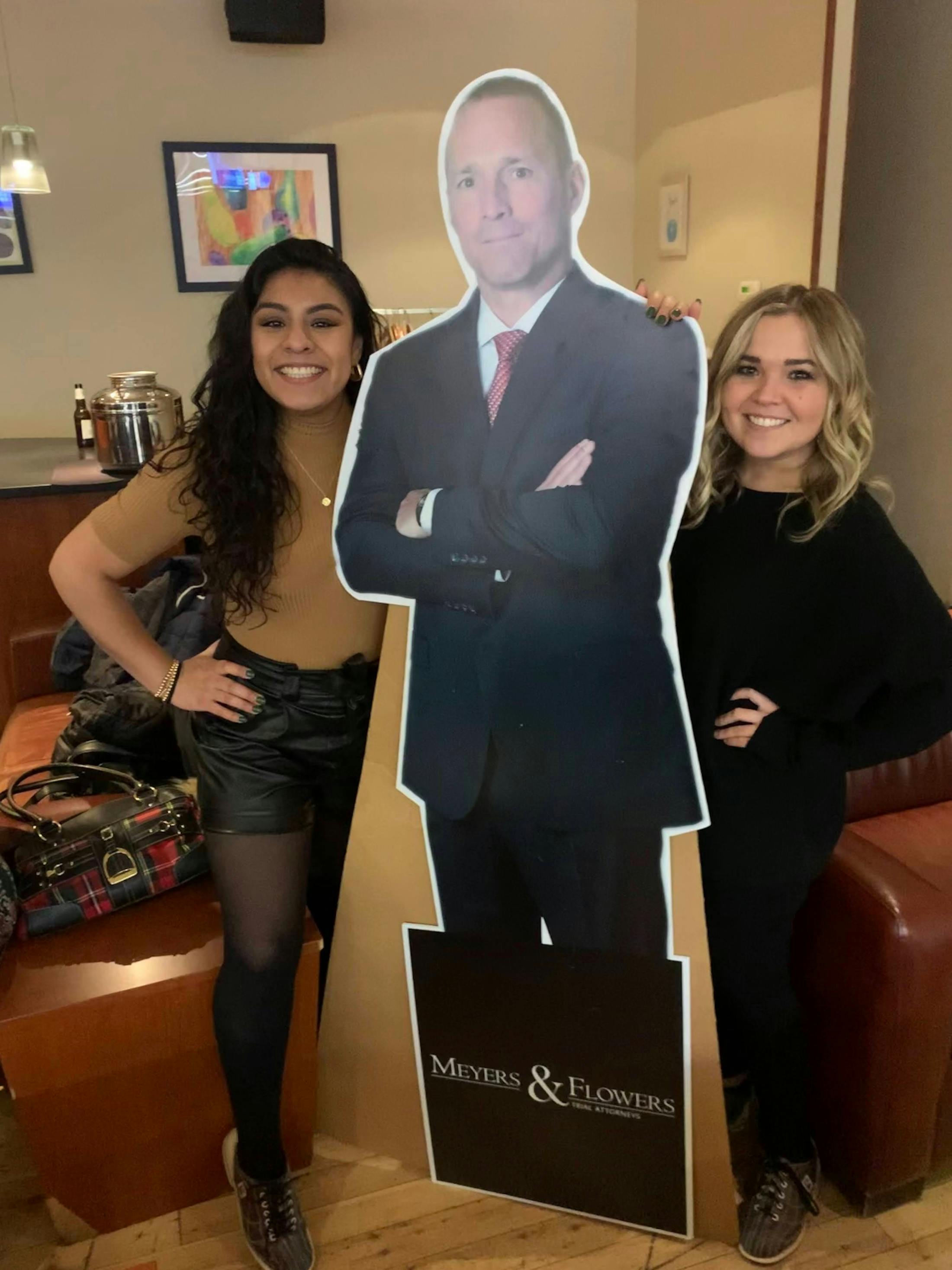 two women standing next to a cardboard cutout of a man