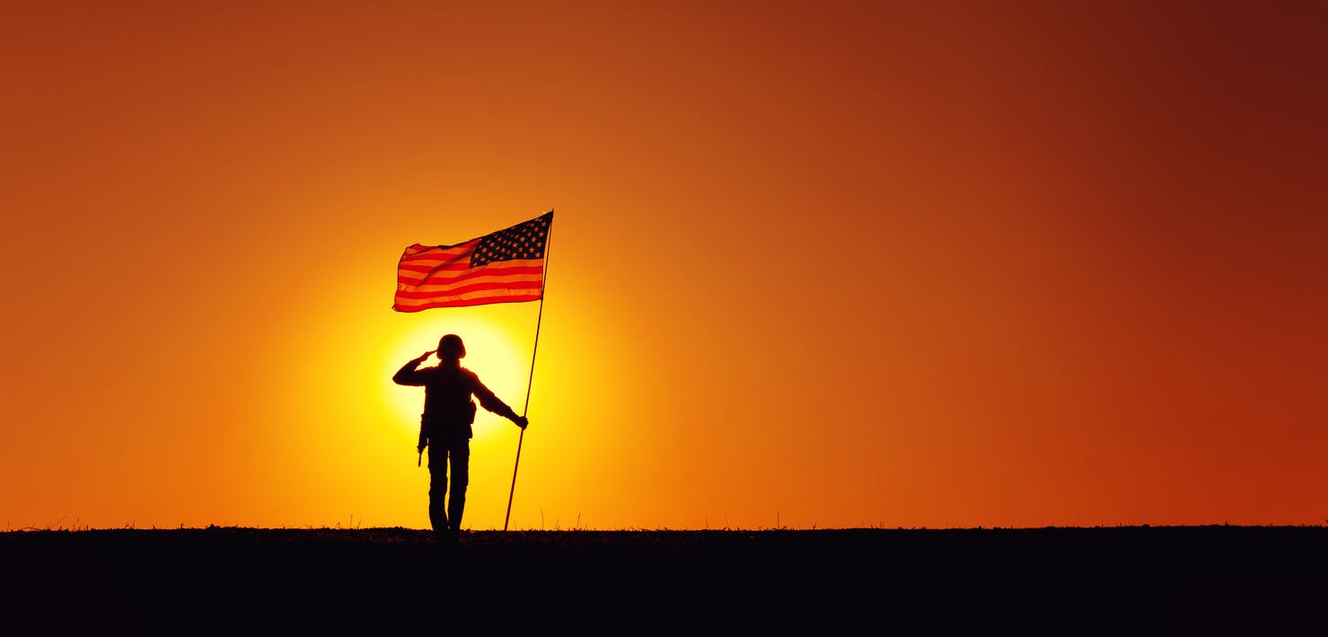 soldier saluting in sunset holding a flag