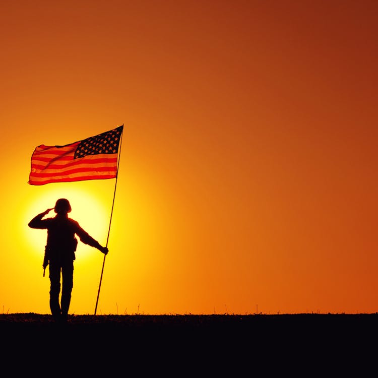 soldier saluting in sunset holding a flag