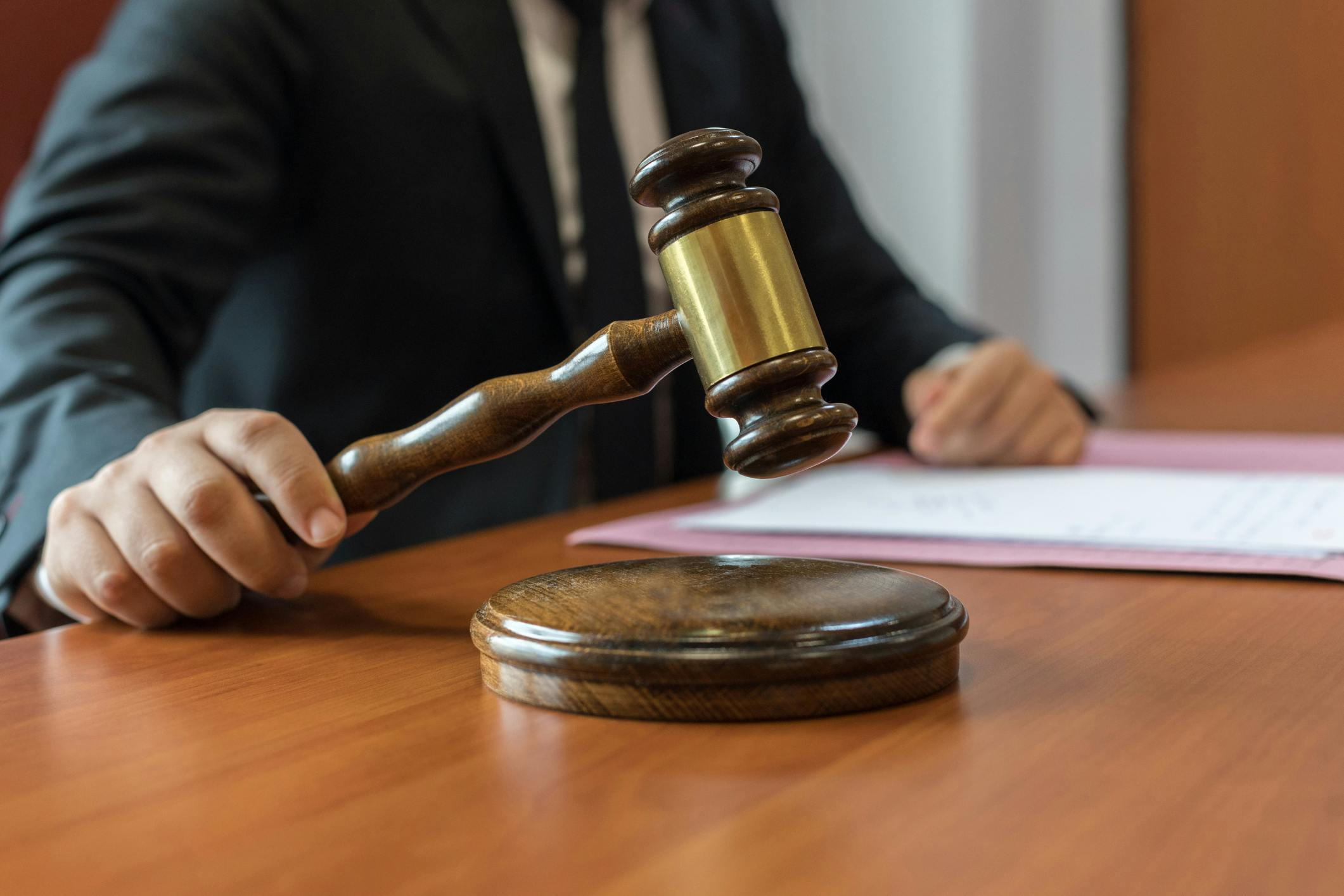 wooden gavel in hand sitting on a desk with a person in a suit