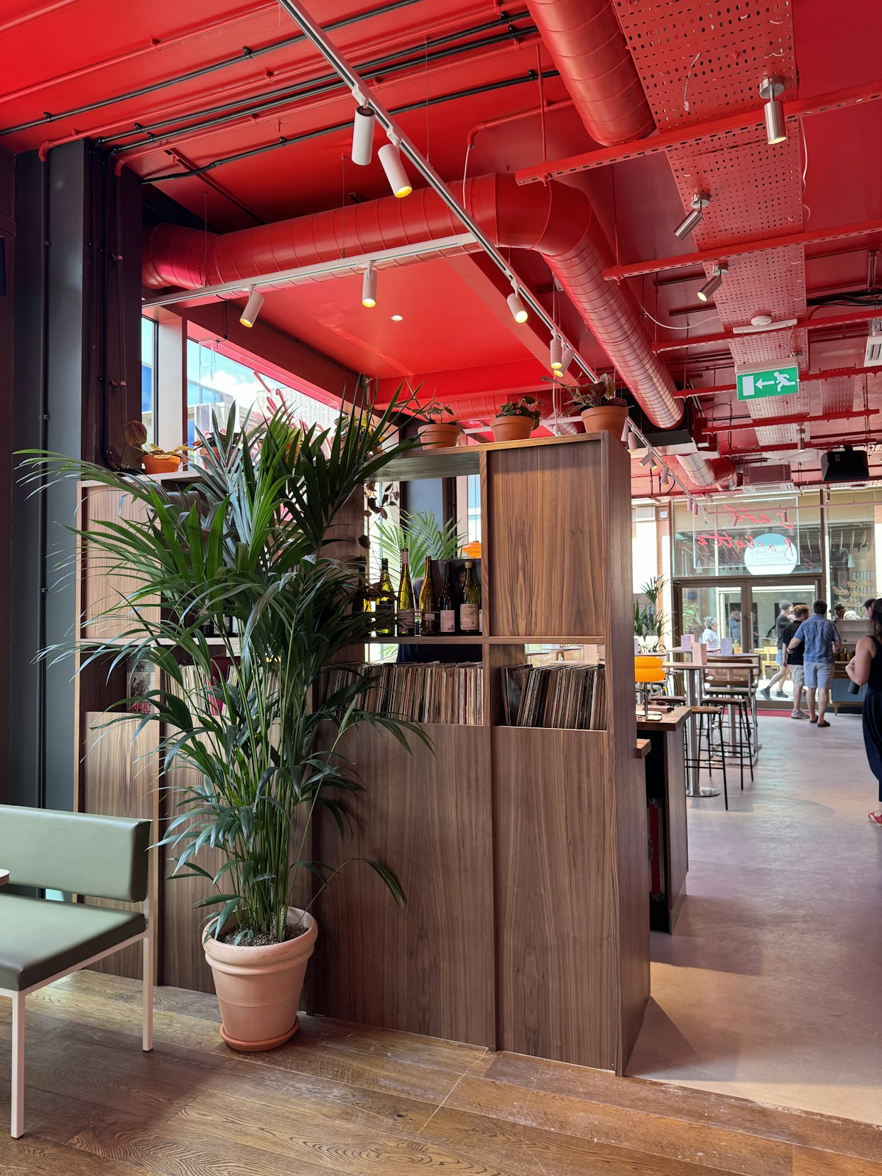 A tall green potted palm plant situated next to a wooden room divider in a modern restaurant interior featuring a bright red industrial ceiling at Barbette, Chester